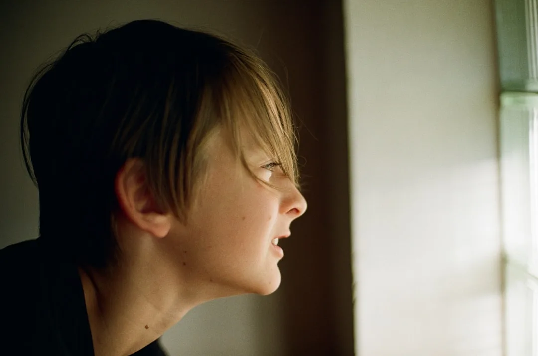 hopeful but tired face looking out window candid natural lighting moody